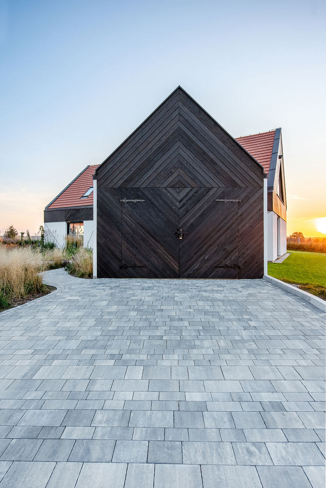 A modern architectural design with a striking black facade, featuring a symmetrical diamond pattern, and a paved walkway leading to the entrance.