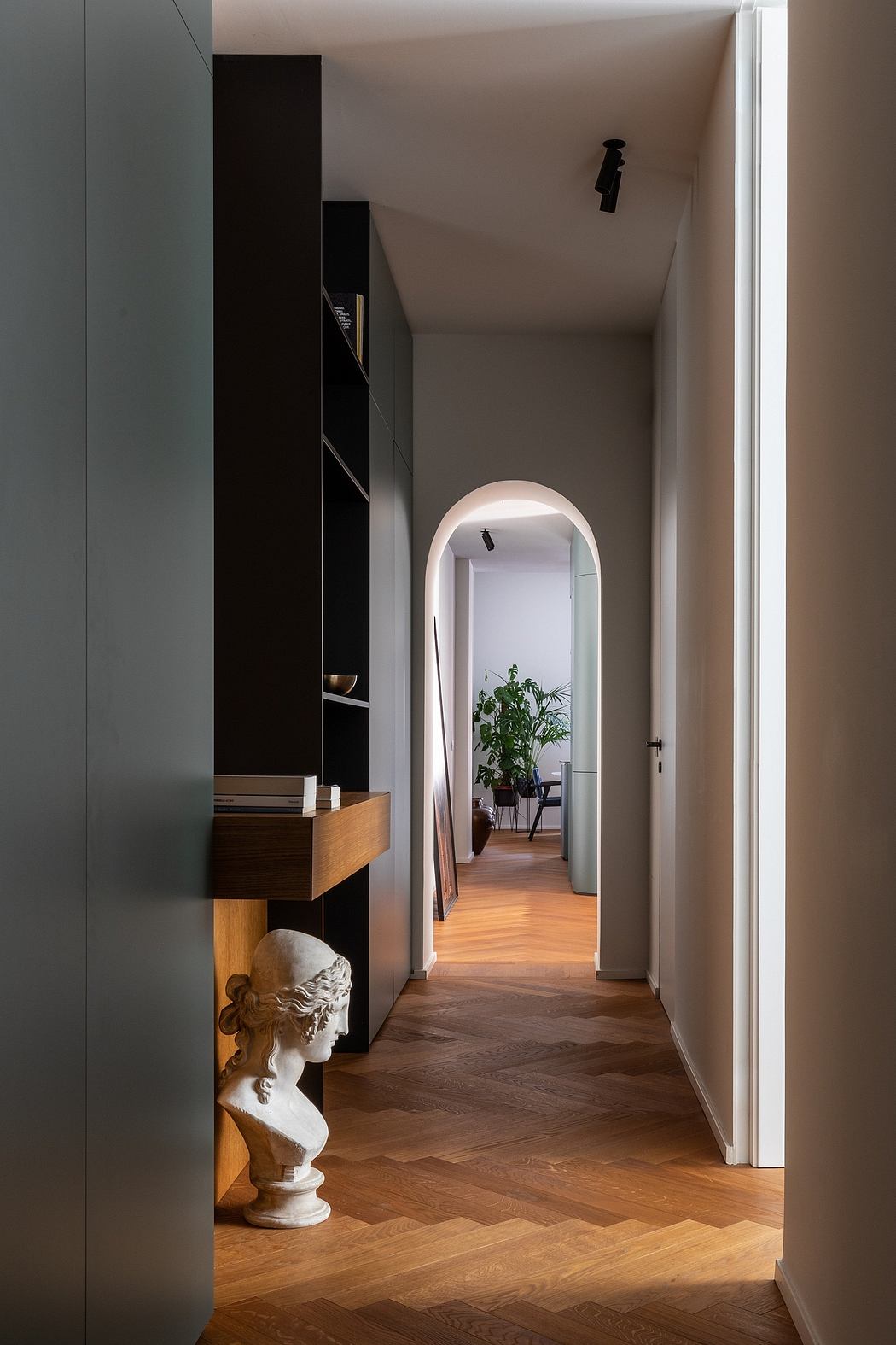 A hallway with a curved entryway, black cabinetry, and a decorative bust on a wooden floor.