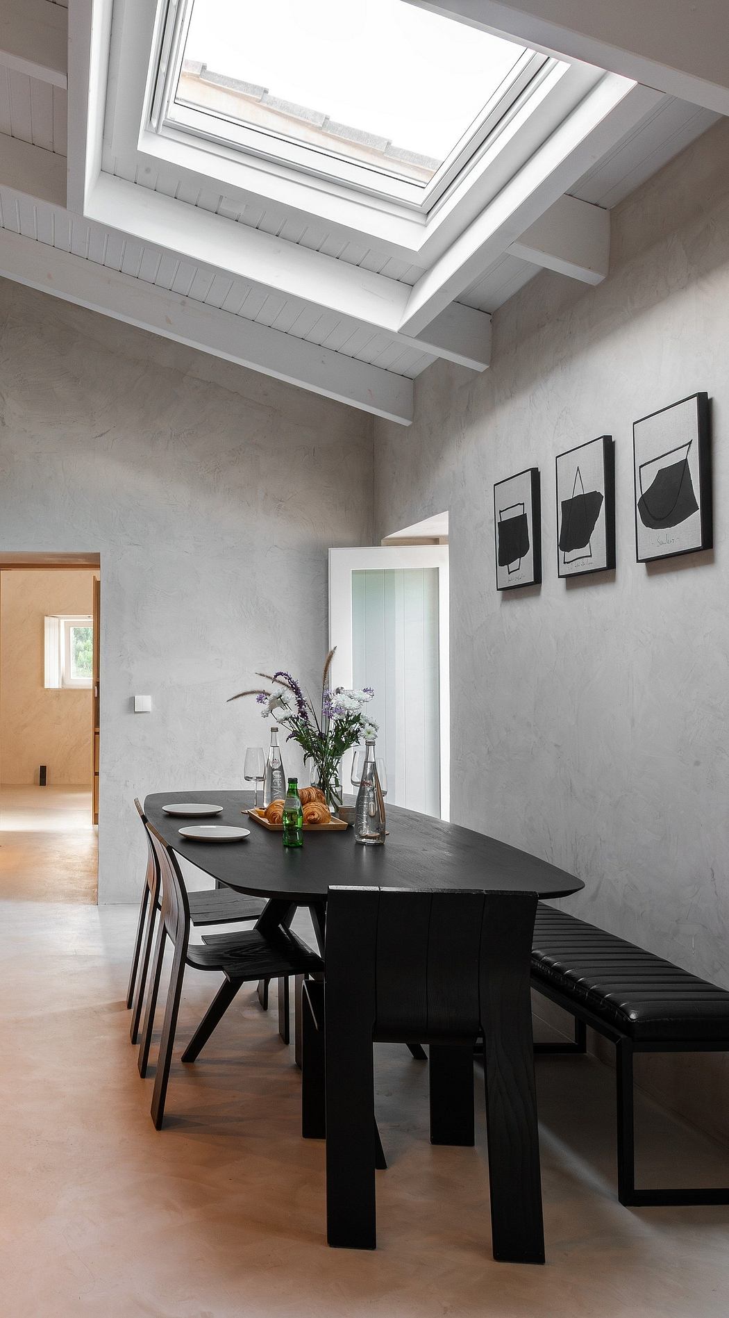 Modern dining area with sleek black table, chairs, and abstract artwork on gray walls. Skylight adds natural light.