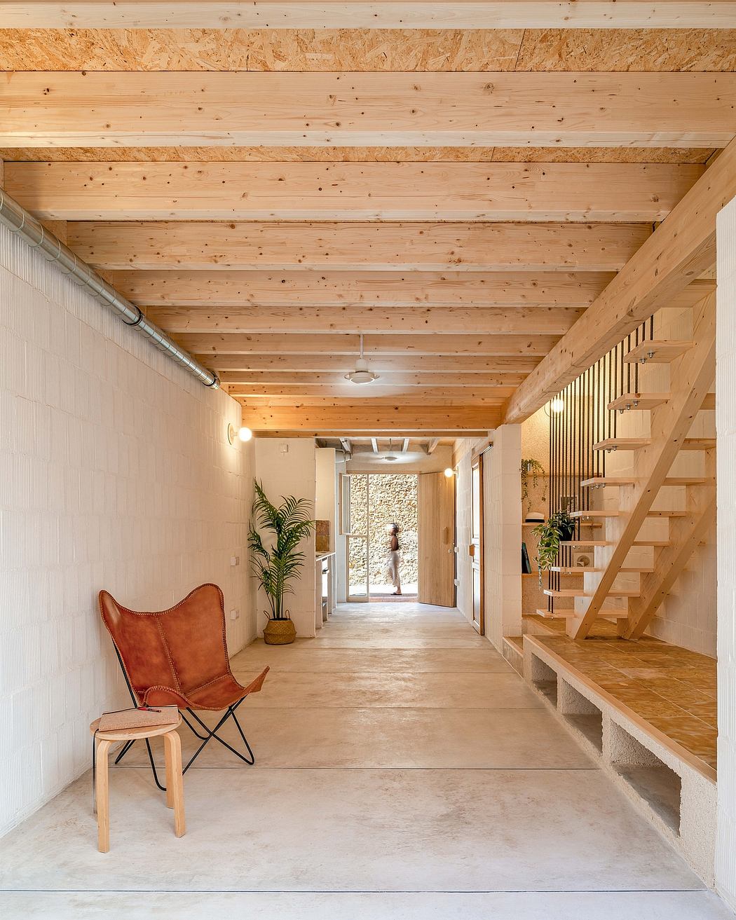 A rustic wooden hallway with a leather armchair, plants, and a staircase leading up.
