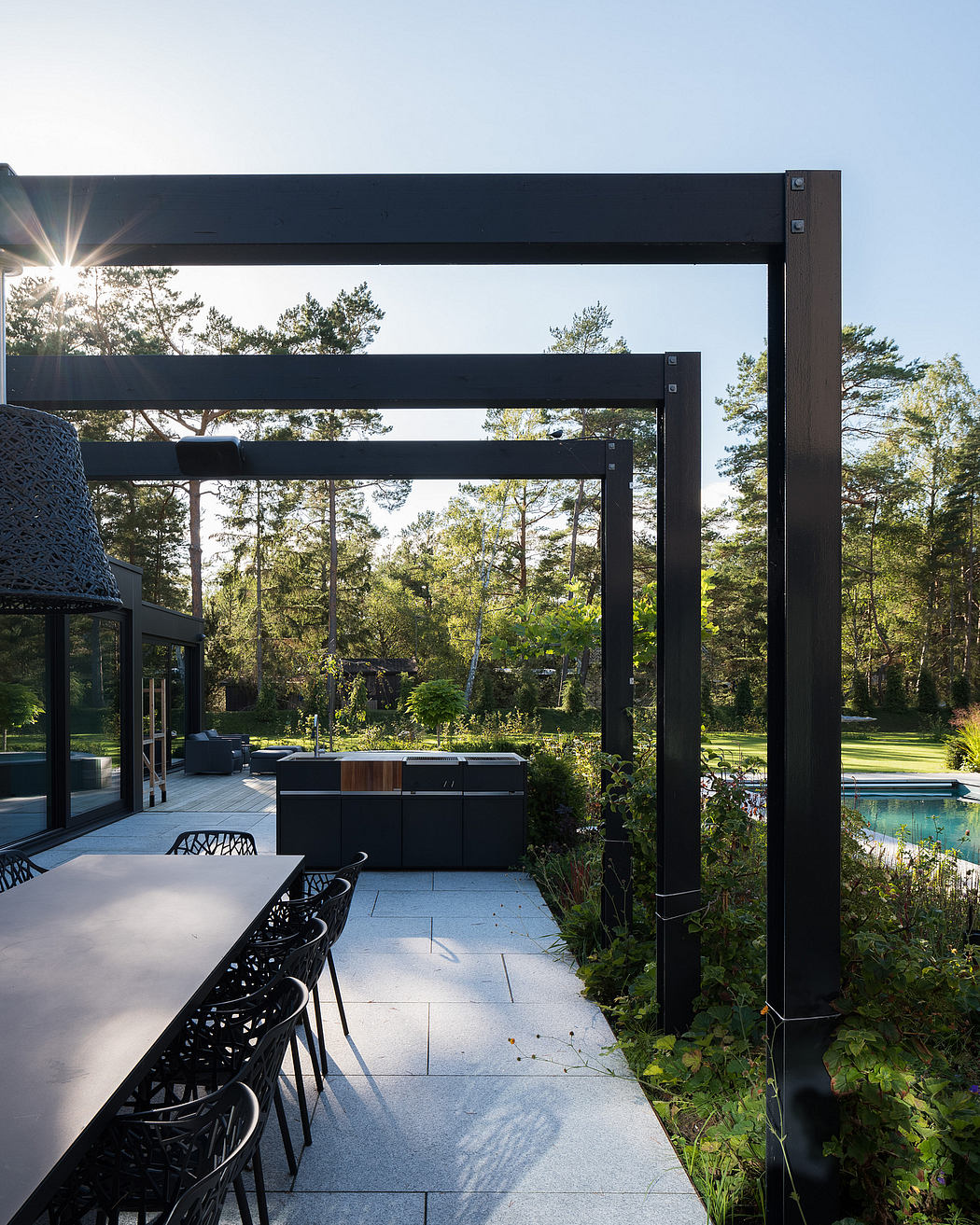 Modern outdoor patio with sleek black metal frames, concrete flooring, and lush green surroundings.