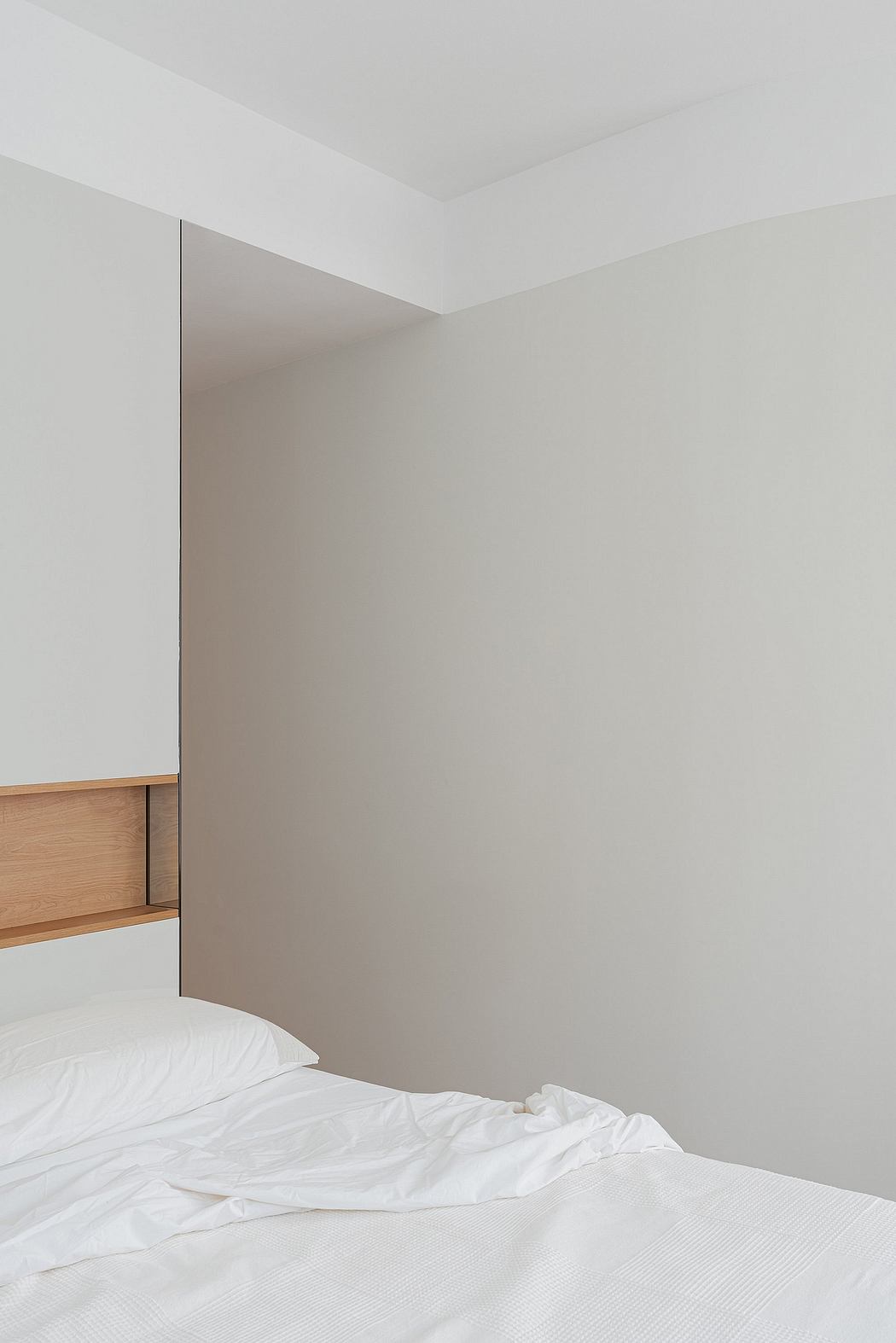 A minimalist bedroom with clean lines, a built-in wood shelf, and a serene white bed.