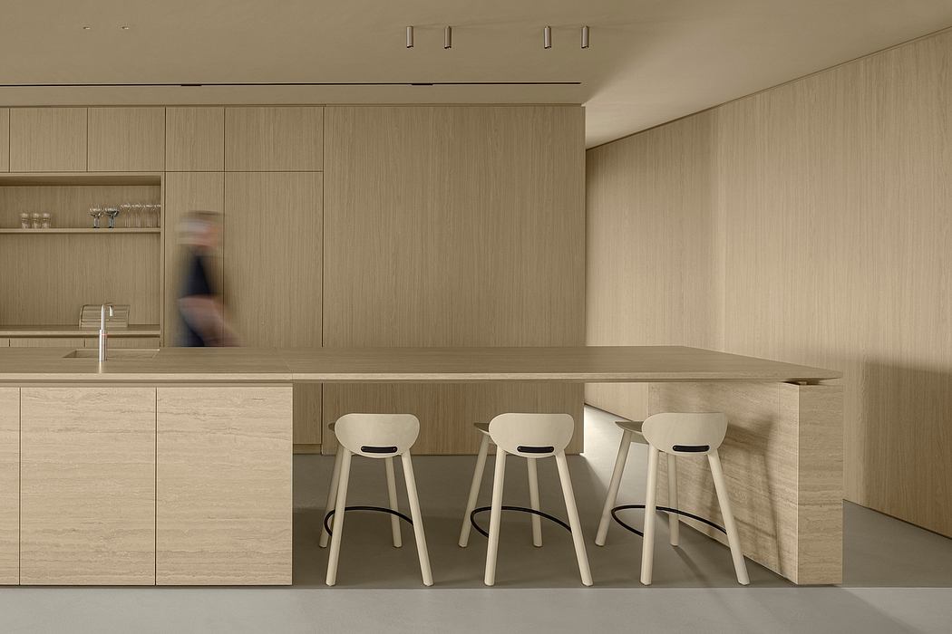 Minimalist kitchen featuring wooden cabinetry, a long counter, and modern white stools.