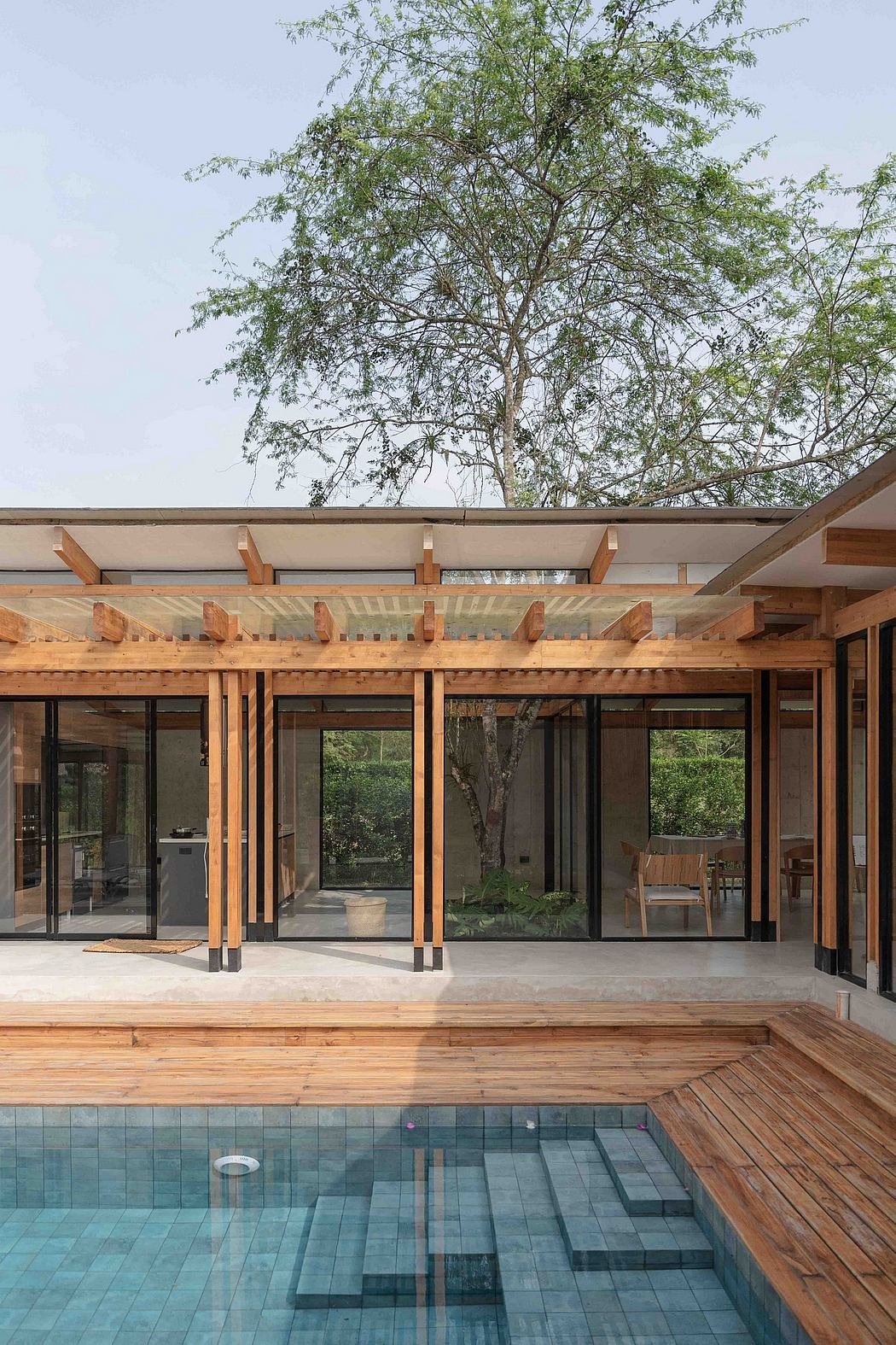 Wooden beams, glass panels, and a tiled pool surrounded by a lush, wooded landscape.