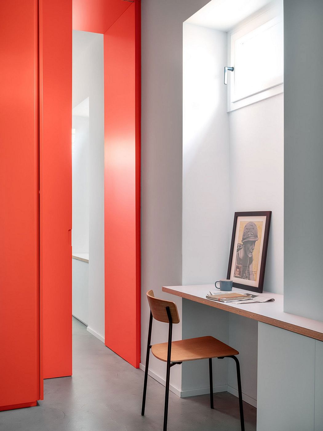 Vibrant red closet doors contrast with muted gray walls, creating a modern look. Sleek desk and chair complete the minimalist design.