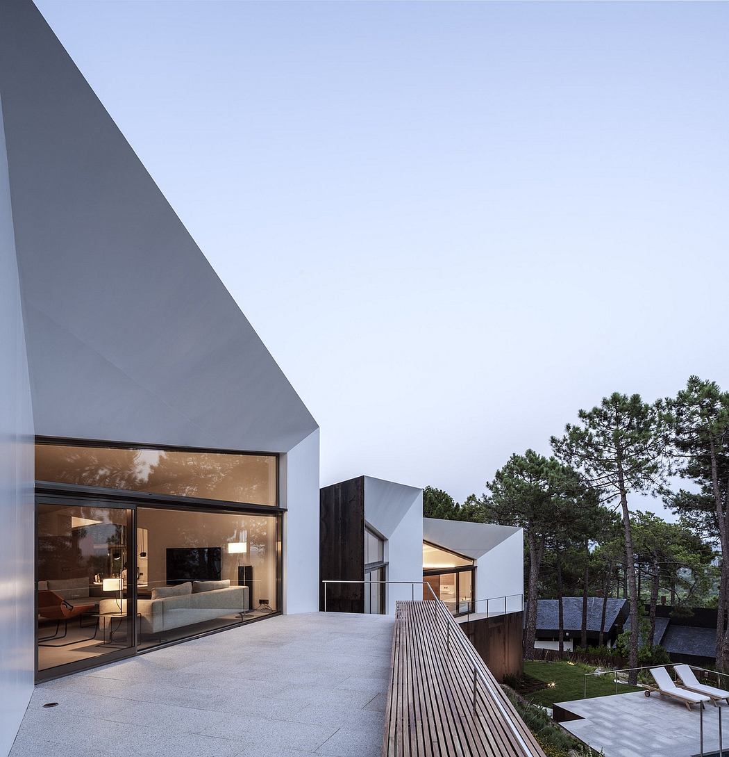 Modern, minimalist architecture with large glass windows overlooking a wooded landscape.
