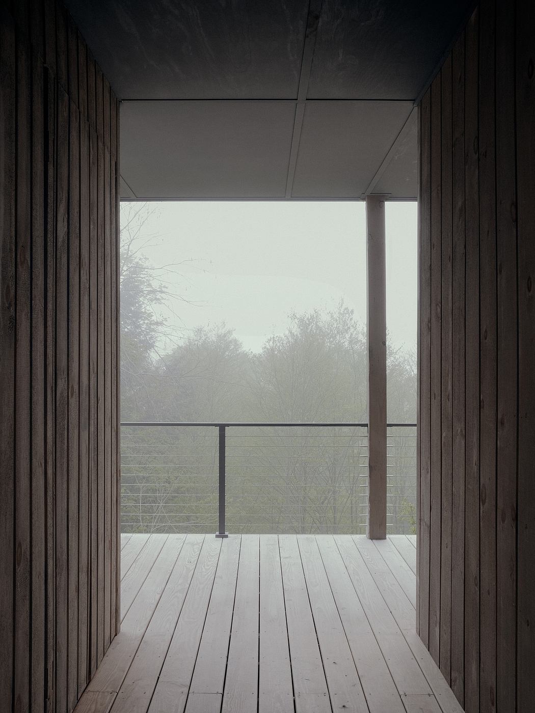Minimalist wooden interior with large windows overlooking a misty outdoor scene.