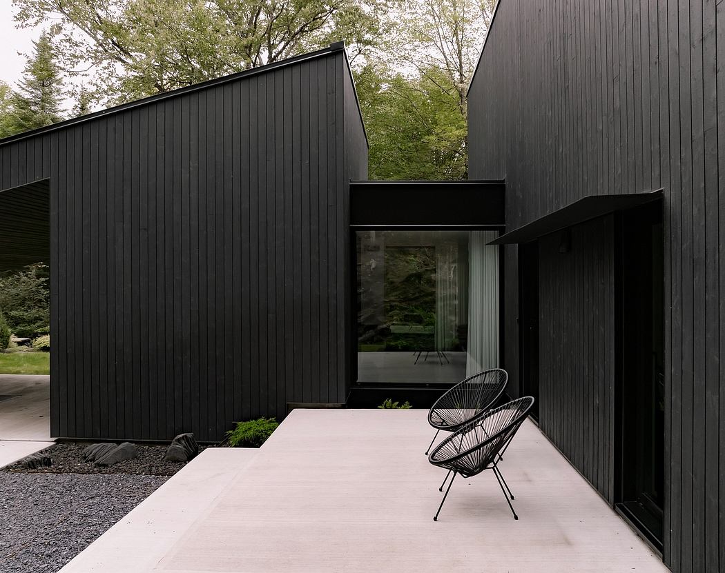 Modern black wooden cabin with sleek design, concrete patio, and minimalist furniture.