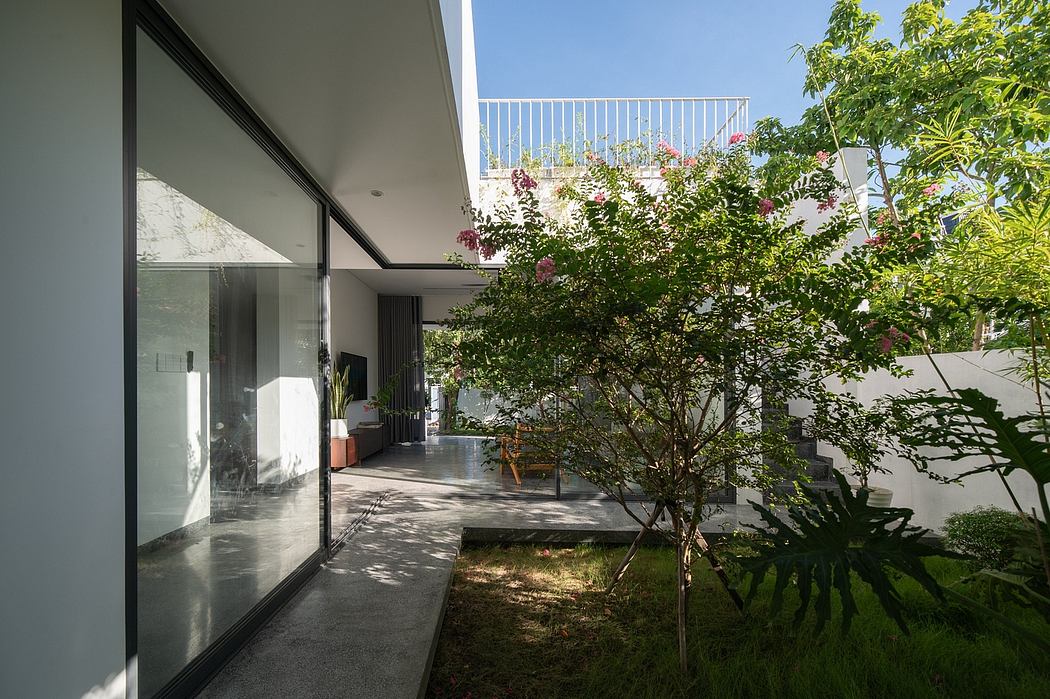 Sleek glass walls, lush greenery, and minimalist patio design create a harmonious indoor-outdoor space.