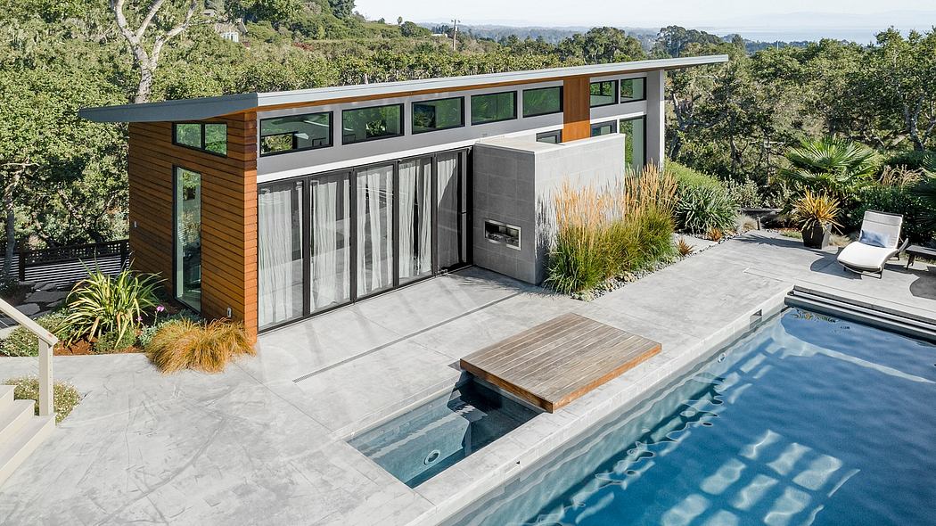 A modern, glass-walled home with a wooden exterior, pool, and lush greenery surrounds.