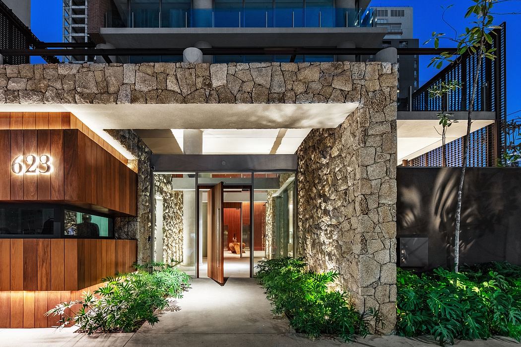 Impressive stone entryway with modern wooden accents and lush greenery framing the entrance.