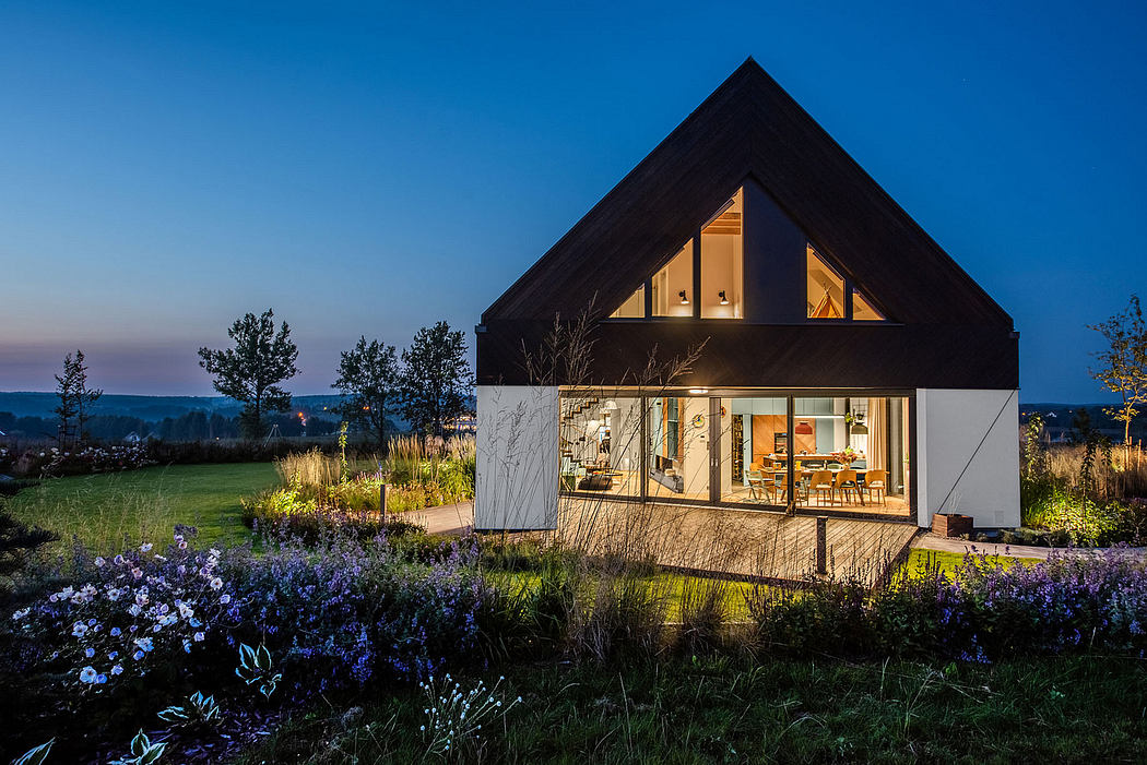 Modern, two-story home with slanted roof, large windows, and outdoor seating area surrounded by lush vegetation.