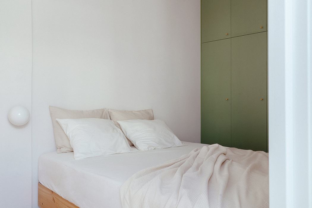 Minimalist bedroom with neutral-toned bedding, built-in green cabinetry, and spherical wall light.
