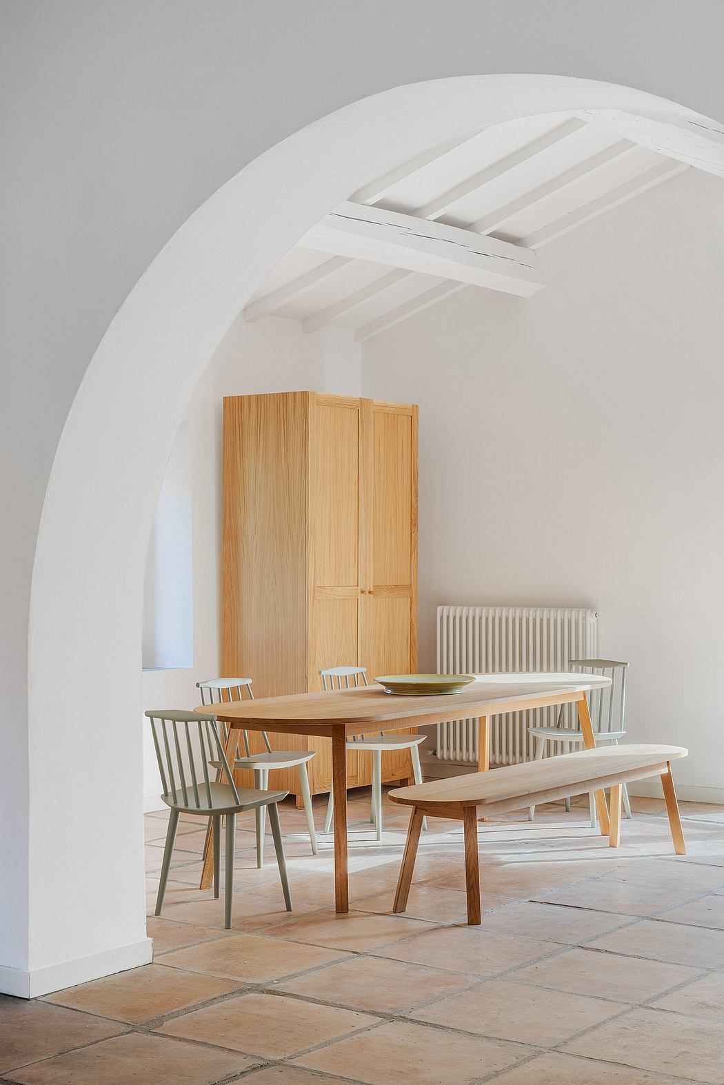A warm, minimalist dining area with wooden furniture, arched ceiling, and tiled flooring.