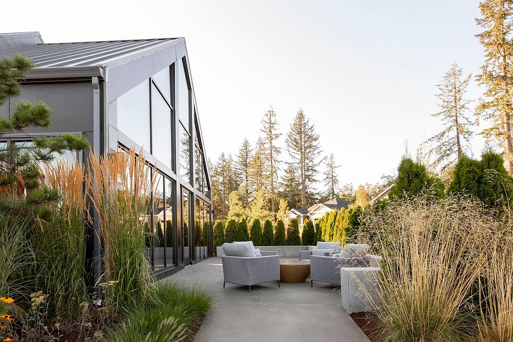 Modern architectural design with a glass facade, patio seating, and lush landscaping.