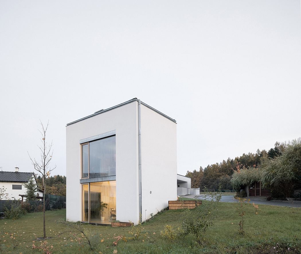 Modern, minimalist house with large windows, glass facade, and grassy surroundings.