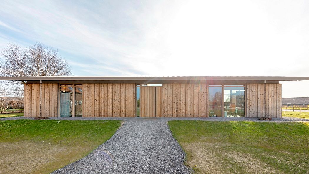 A modern wooden structure with large windows, a gravel path, and a grassy lawn.
