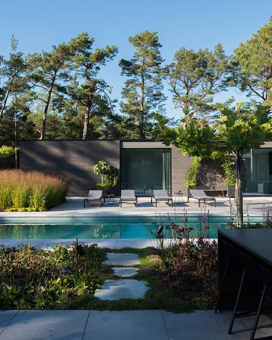 Sleek, modern outdoor space with a pool, lounge chairs, and lush greenery surrounding.