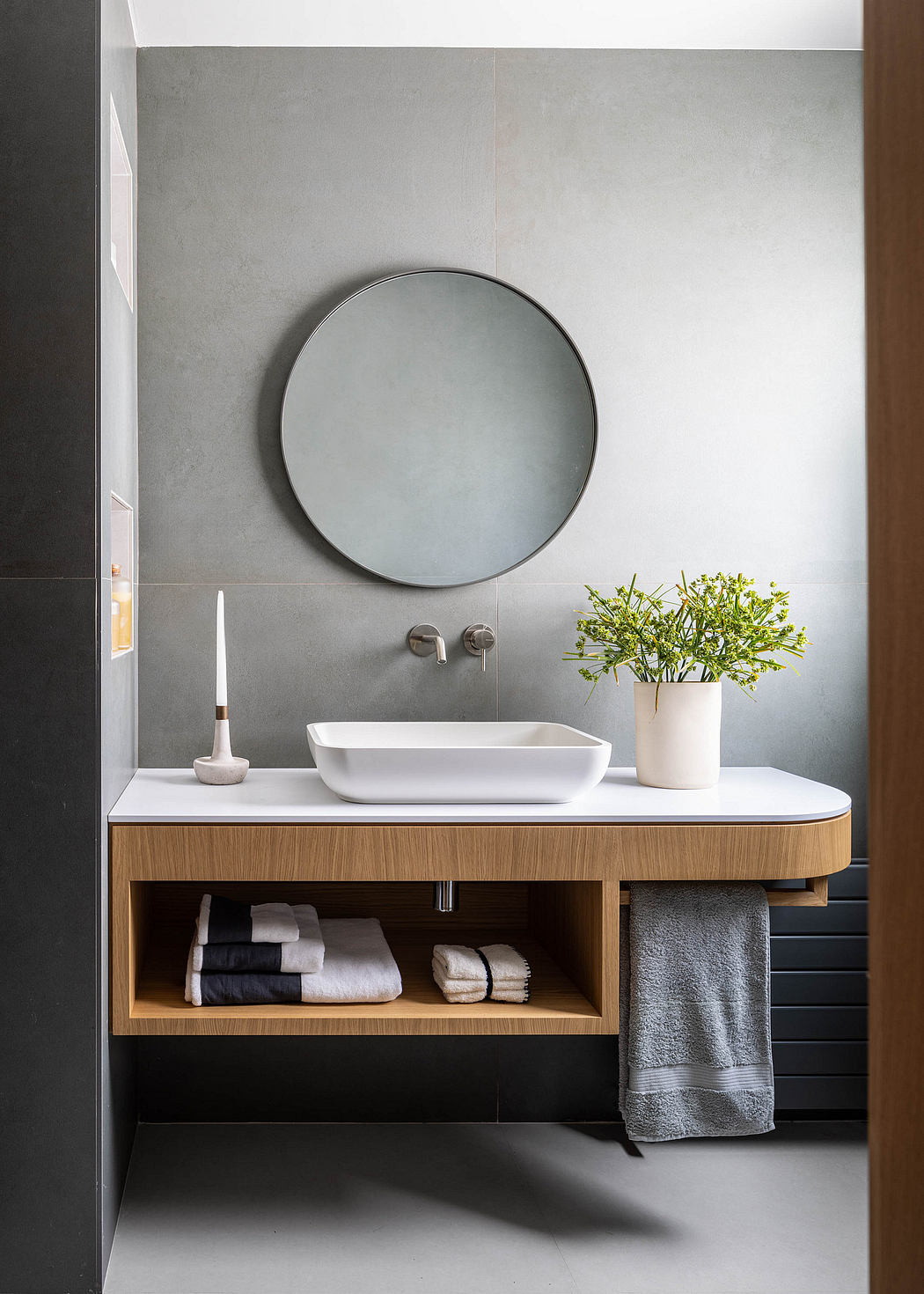 Minimalist bathroom design with white vessel sink, round mirror, and wooden vanity.
