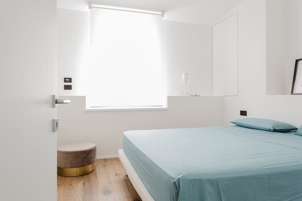 Minimalist bedroom with large window, white walls, wood floors, and sleek furniture.