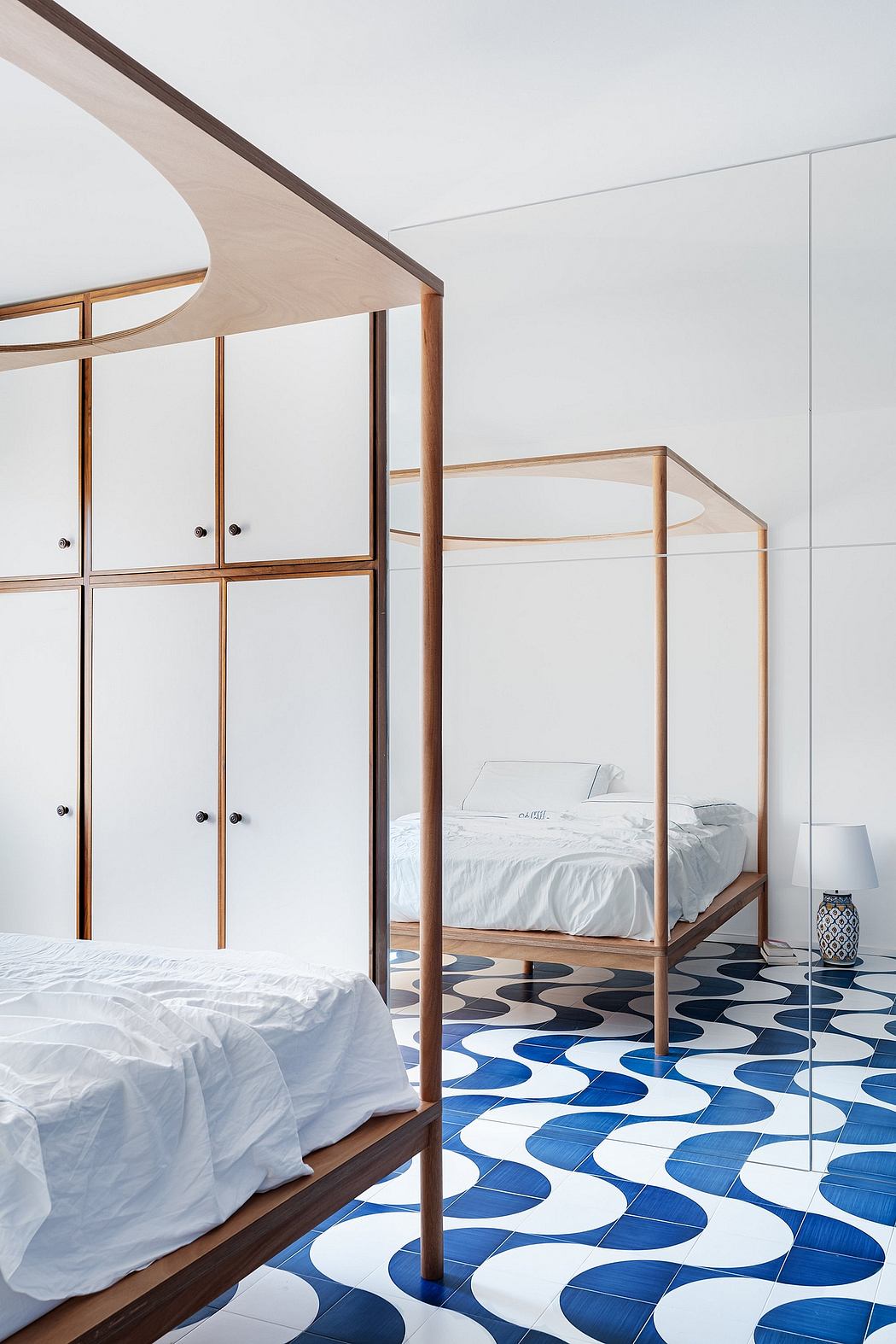 Sleek, wooden canopy bed frame and built-in cabinets. Patterned tile flooring in shades of blue.