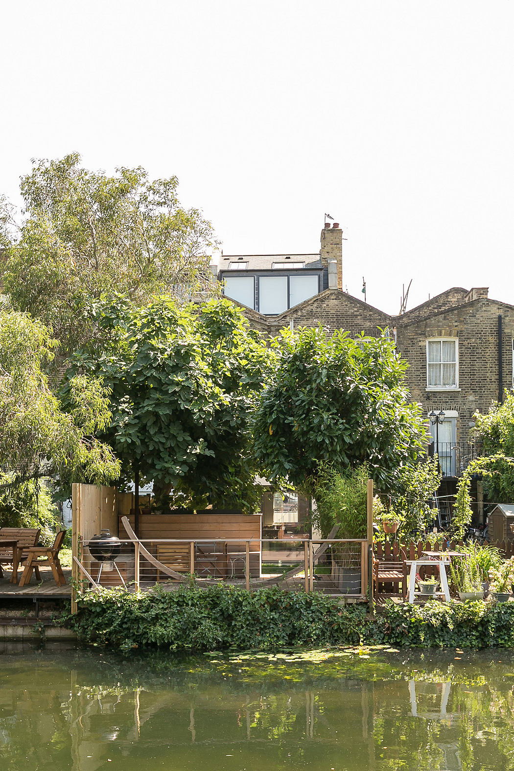 Serene urban oasis with a lush green garden, wooden deck, and calm reflecting pond.