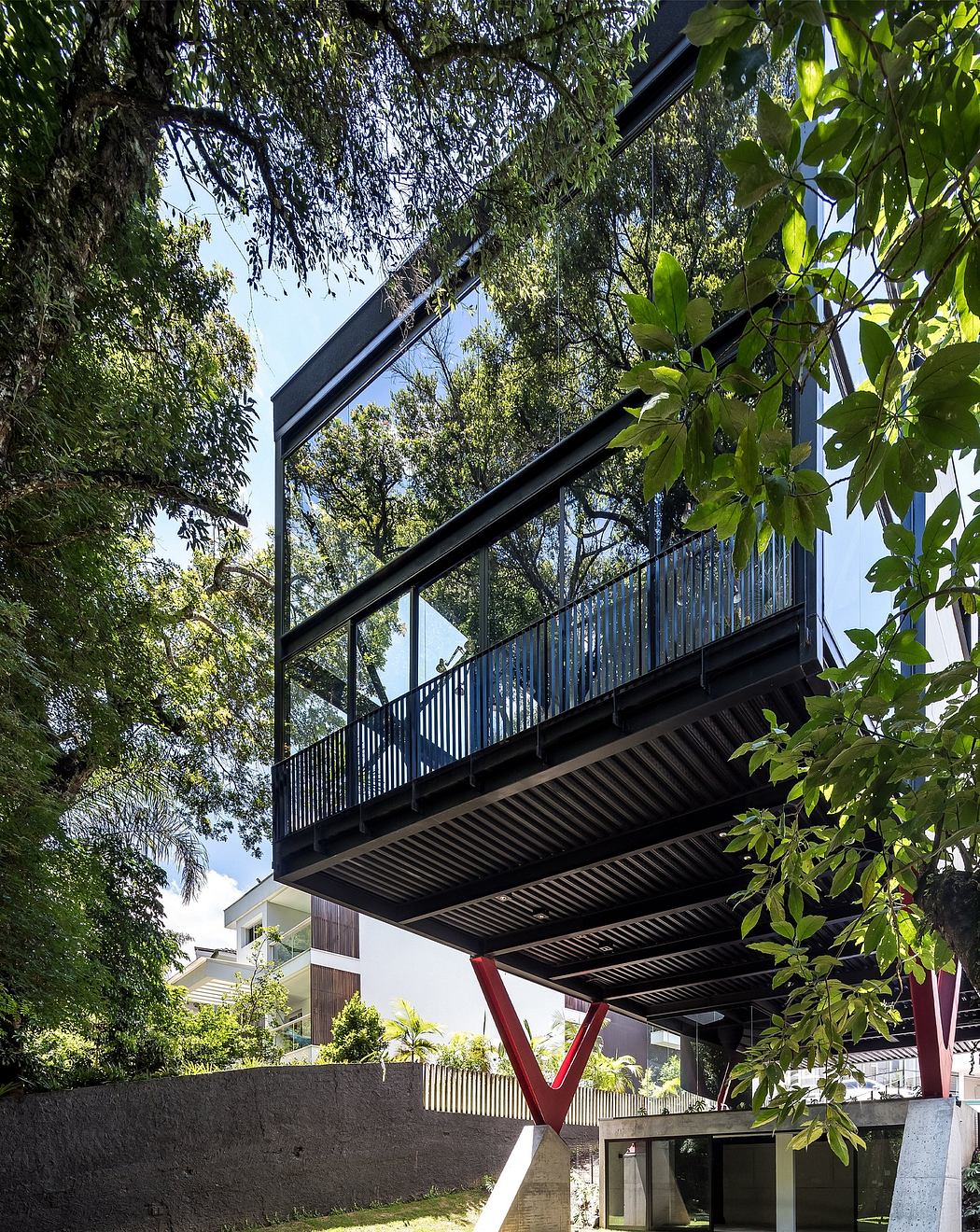 A modern, elevated walkway with a sleek, black steel frame and glass balustrade, surrounded by lush greenery.