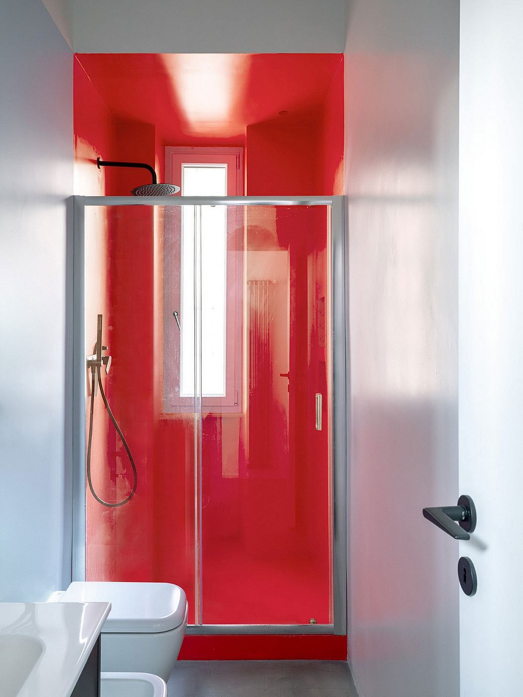 Vibrant red bathroom with sliding glass shower door and minimalist fixtures.