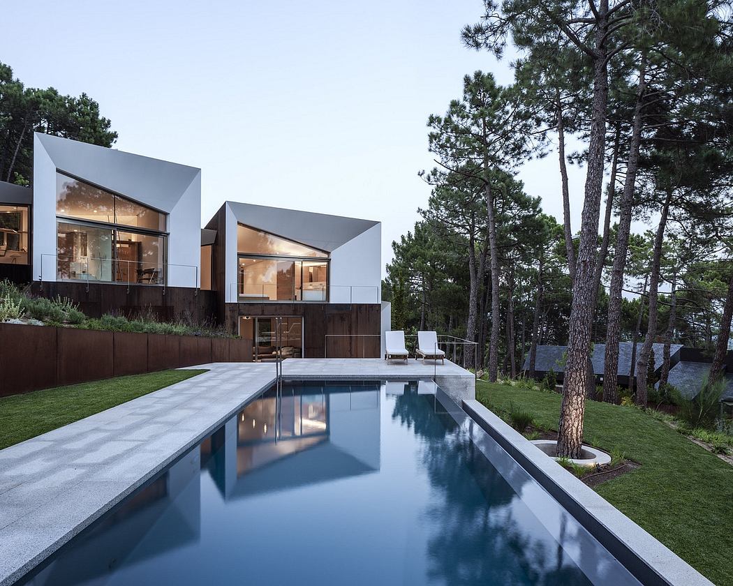 Modern modular home with sleek glass walls, reflecting pool, and pine trees.