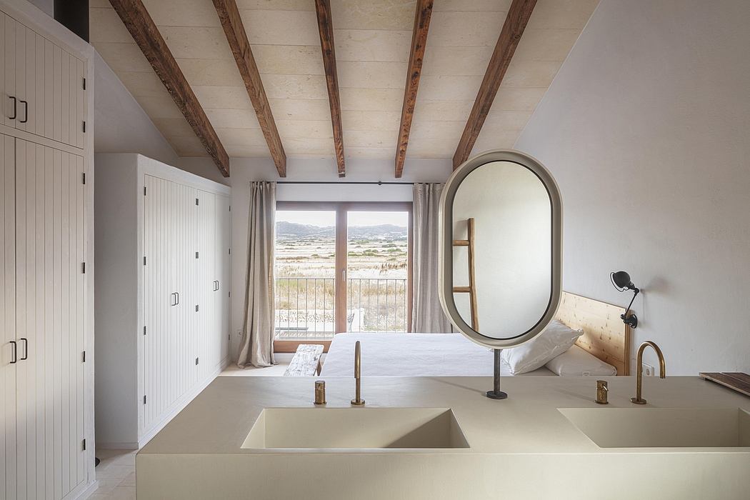 Rustic beamed ceiling, arched window, minimalist vanity, and oval mirror in bedroom.
