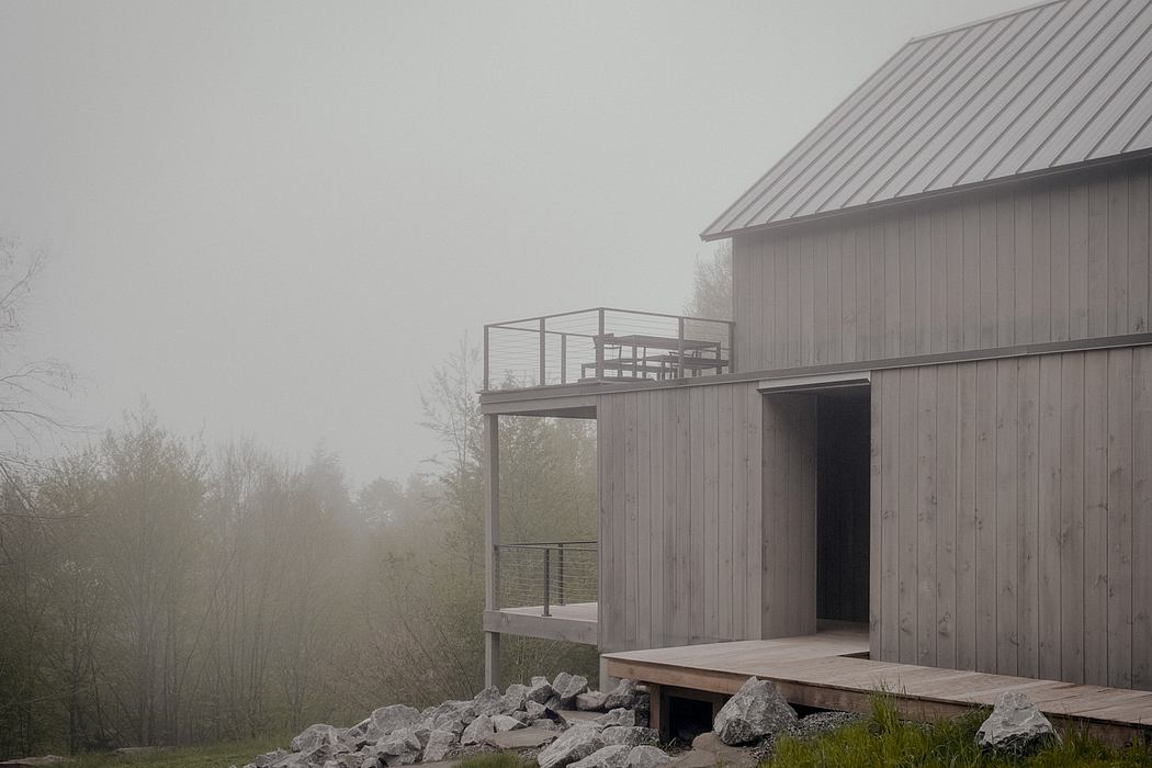A modern, wooden structure with a cantilevered deck and metal railings, situated in a misty forest.