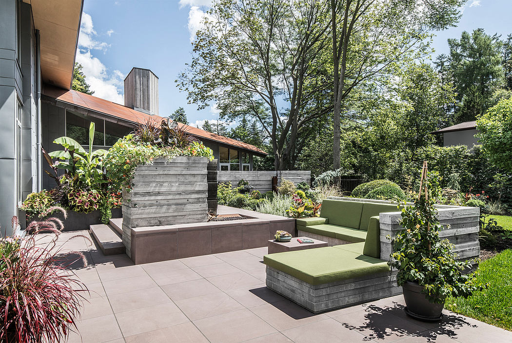 Outdoor patio area with modern, geometric seating and lush plantings against a wooded backdrop.
