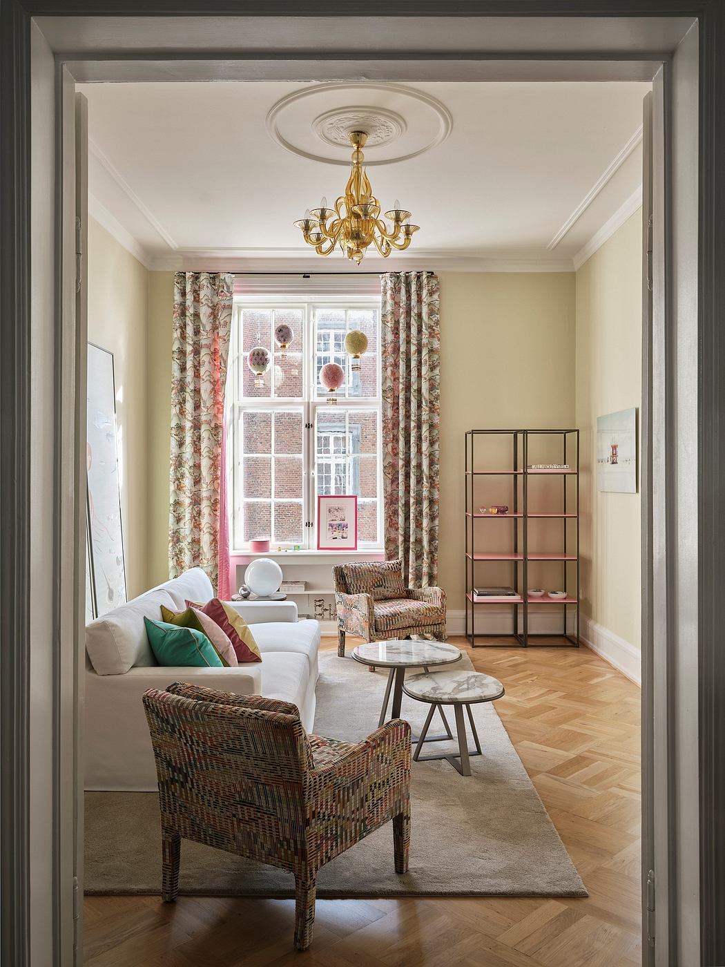 Ornate ceiling molding, brass chandelier, floral curtains, and woven furniture.