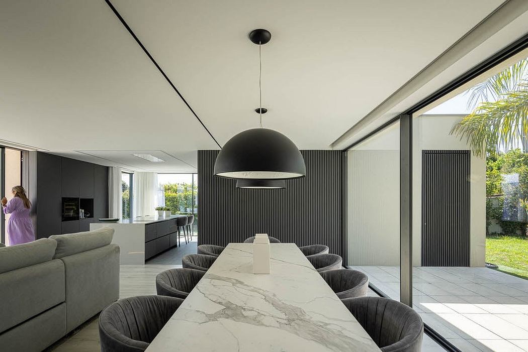 Minimalist open-concept living space with marble dining table, dark furnishings, and floor-to-ceiling windows.