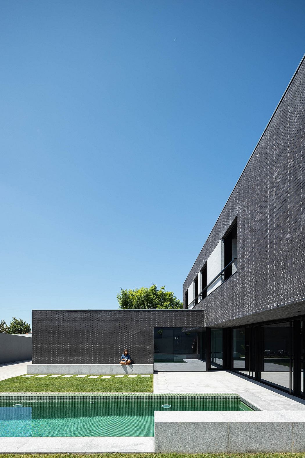 Striking black brick building with a green pool and lush greenery.