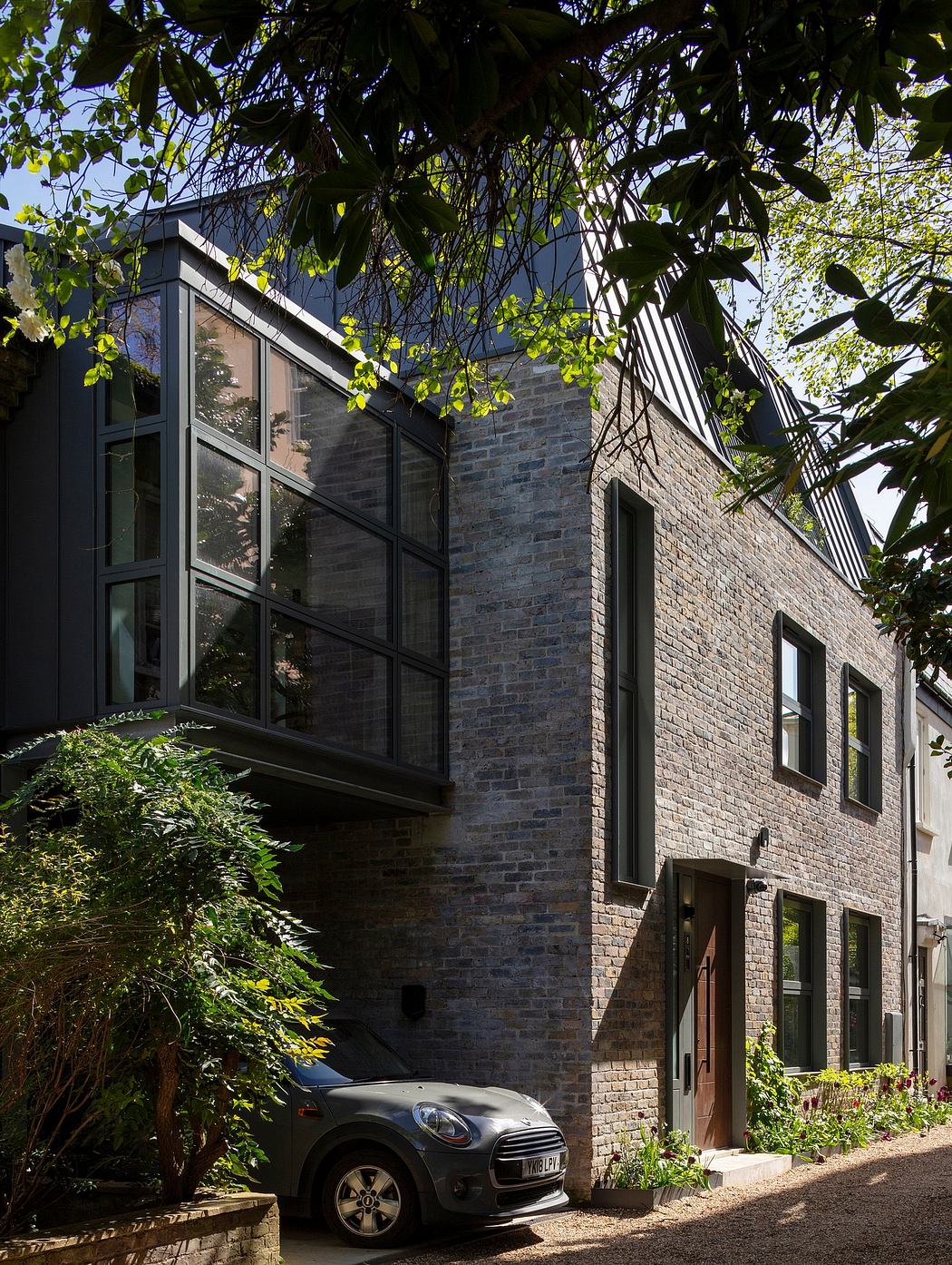 A modern brick building with large windows, surrounded by lush greenery.