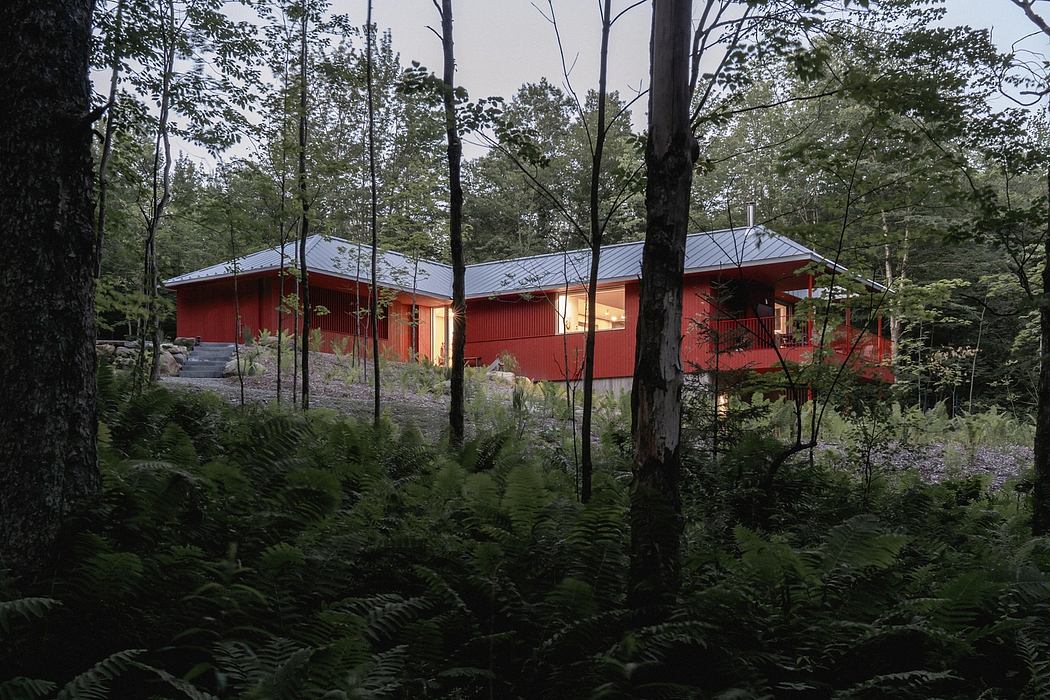 A red wooden cabin nestled amongst lush greenery and towering trees.