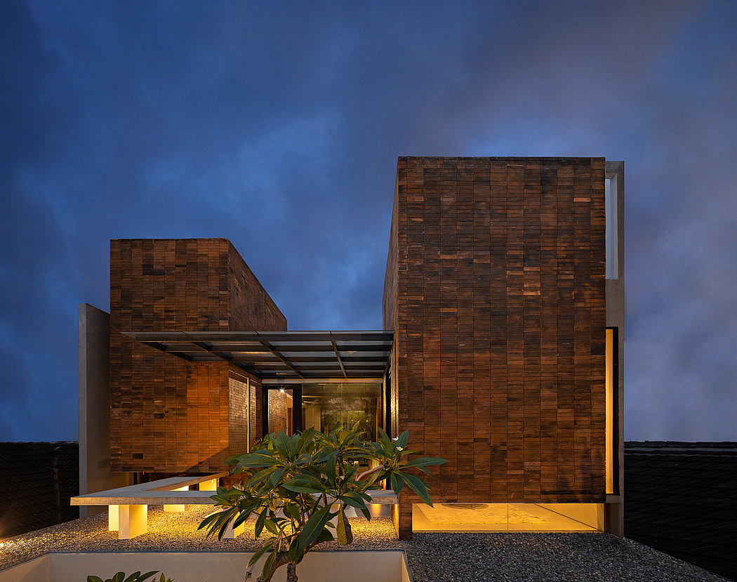 A modern, wooden-clad building with a glass entryway, surrounded by lush greenery.