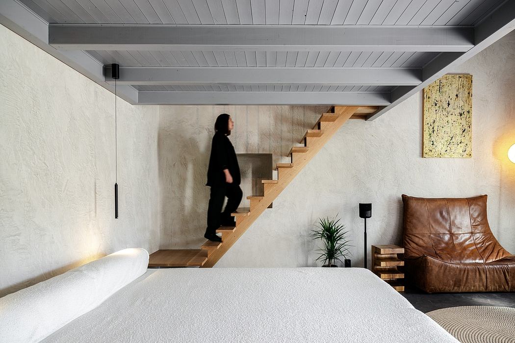 A modern, minimalist interior with wooden beams, stairs, and a leather chair.