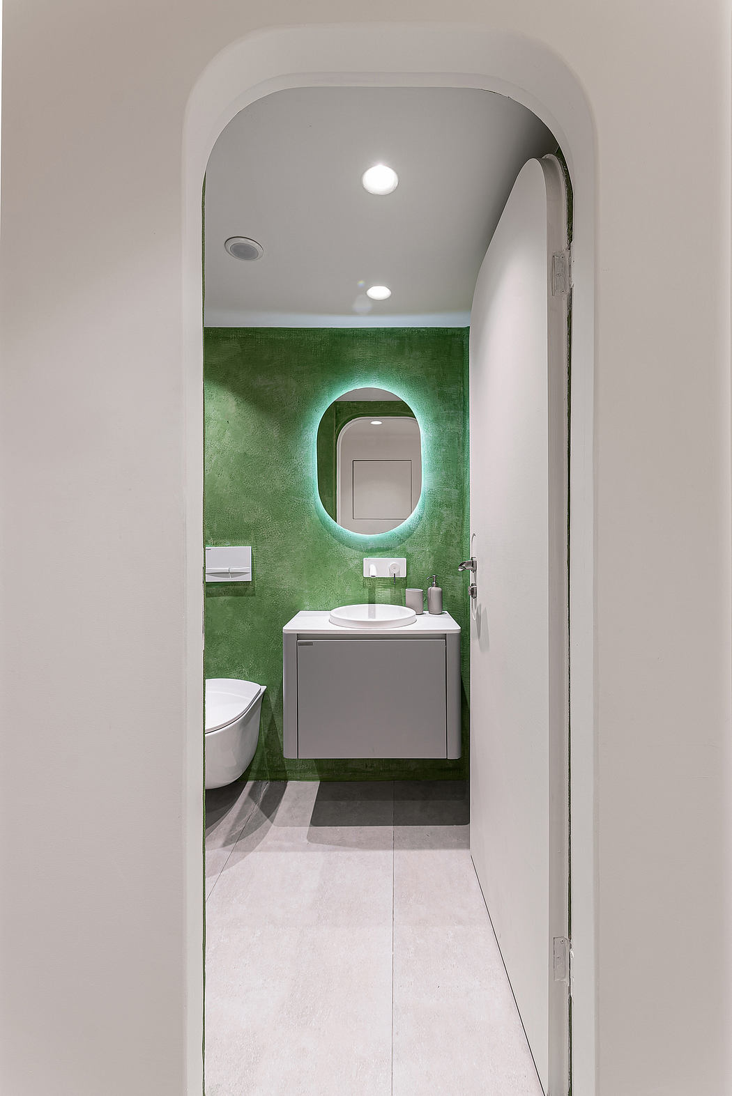 Minimalist bathroom with green accent wall, recessed lighting, and grey vanity.