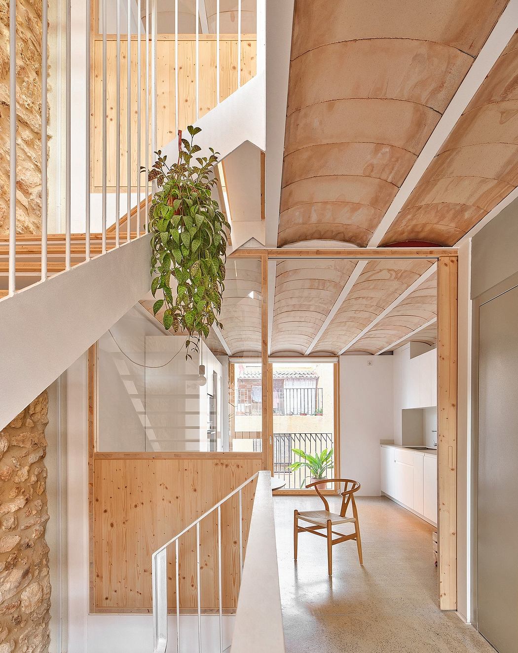 A minimalist, wood-framed interior with curved ceilings, natural light, and a potted plant.
