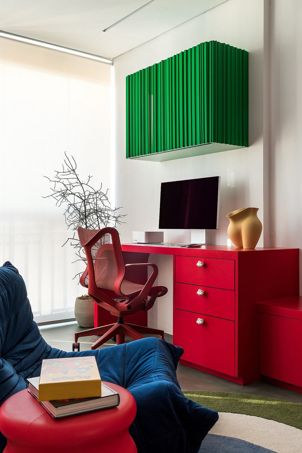 A vibrant, modern workspace with bold red furniture, green shelving, and natural decor.