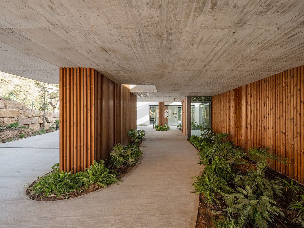 A rustic walkway with wooden slat walls, surrounded by lush greenery, leading to a modern interior.