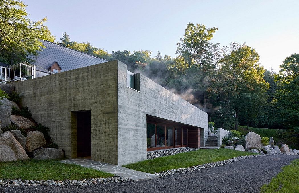 A modern, concrete building with large windows nestled in a wooded, mountainous landscape.