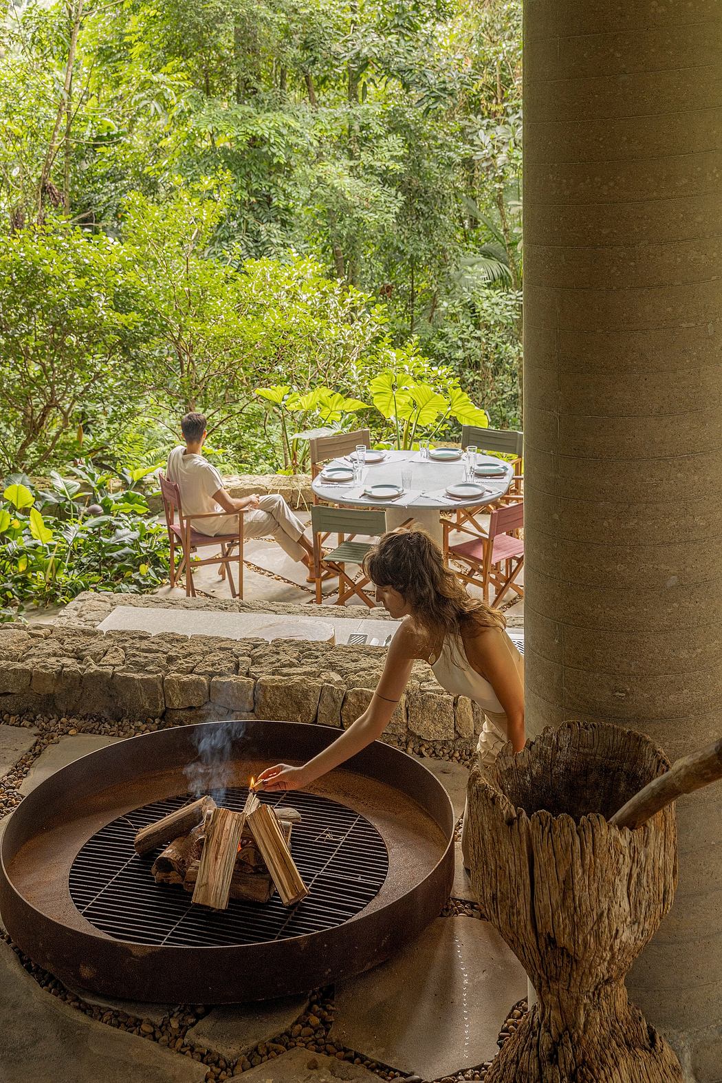 Outdoor dining area surrounded by lush greenery, with a fire pit and rustic stone walls.