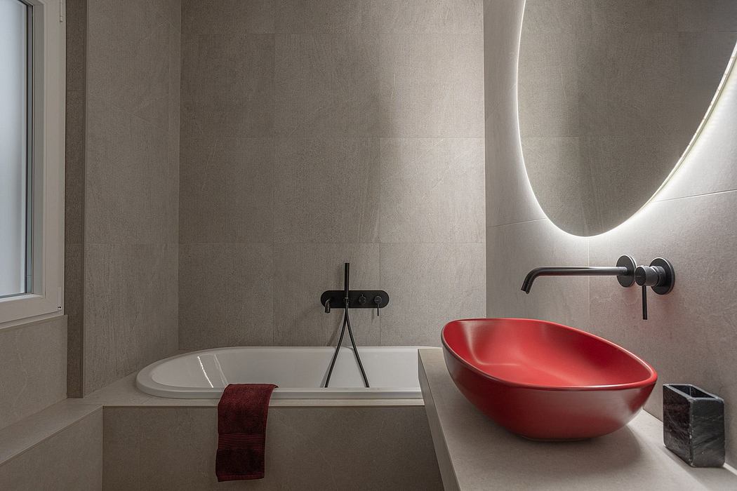 Modern bathroom with curved red ceramic sink basin, oval tub, and illuminated mirror.