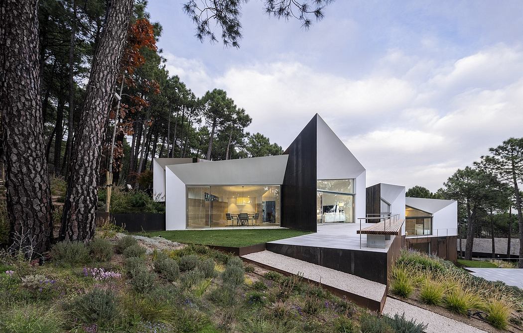 A modern, angular home with large glass walls overlooking a lush, natural landscape.