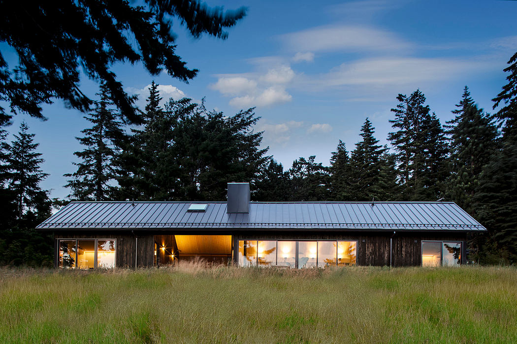 A rustic, wooden cabin nestled in a forested landscape, with large windows and a metal roof.