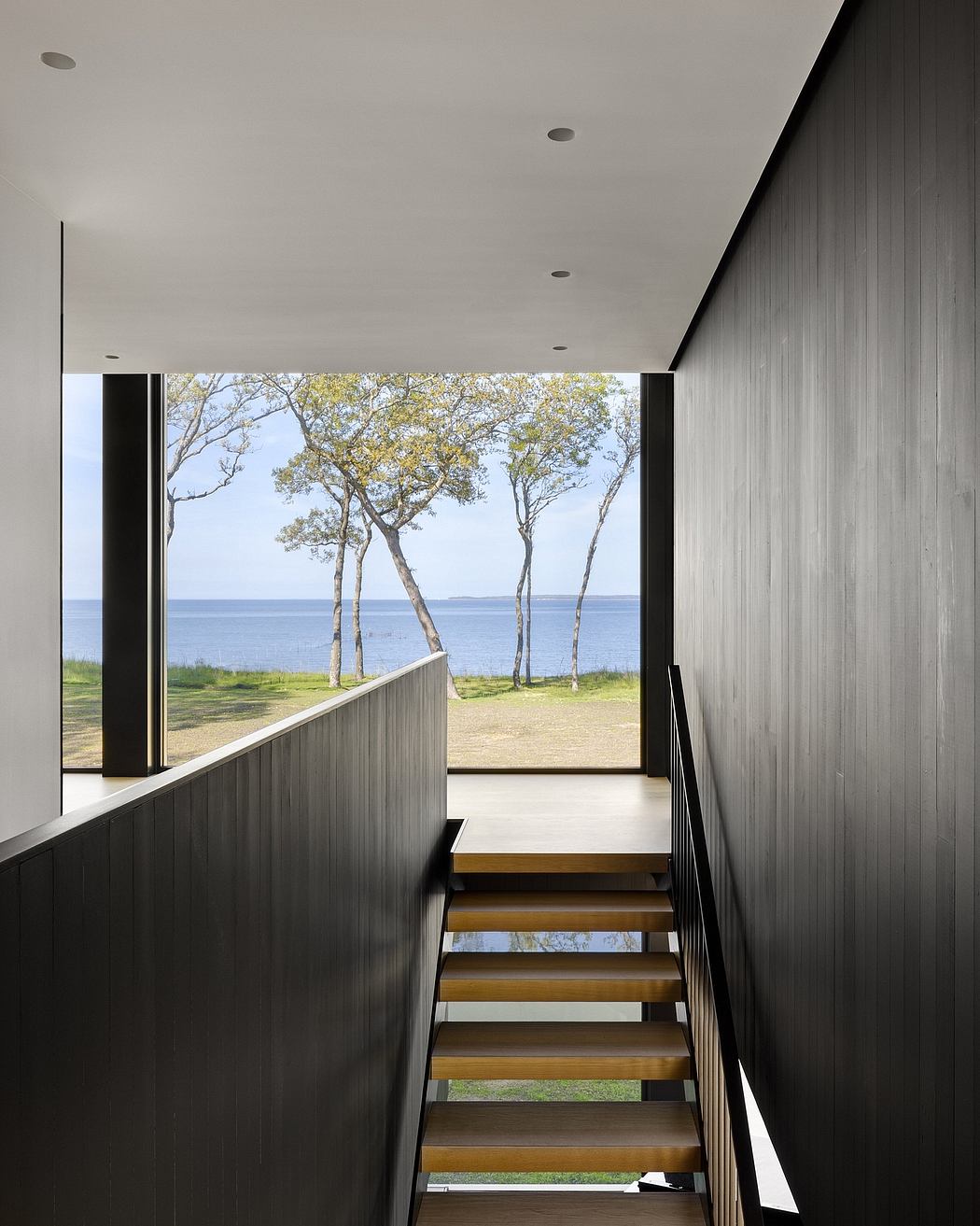 Sleek, modern stairs lead to a panoramic view of lush trees and a tranquil lake.