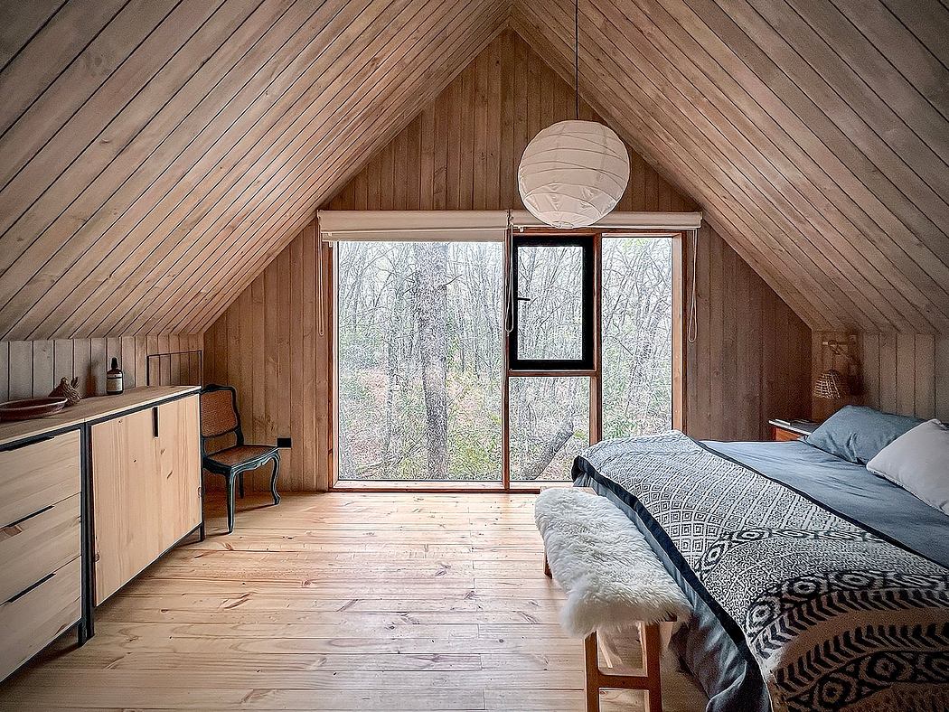Cozy A-frame cabin interior with wood-paneled walls, large window, and rustic furnishings.